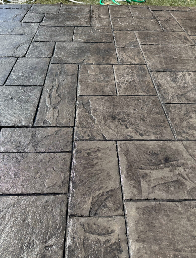 Des Moines sidewalk replacement: Stamped concrete patio with a stone texture and dark gray coloring.