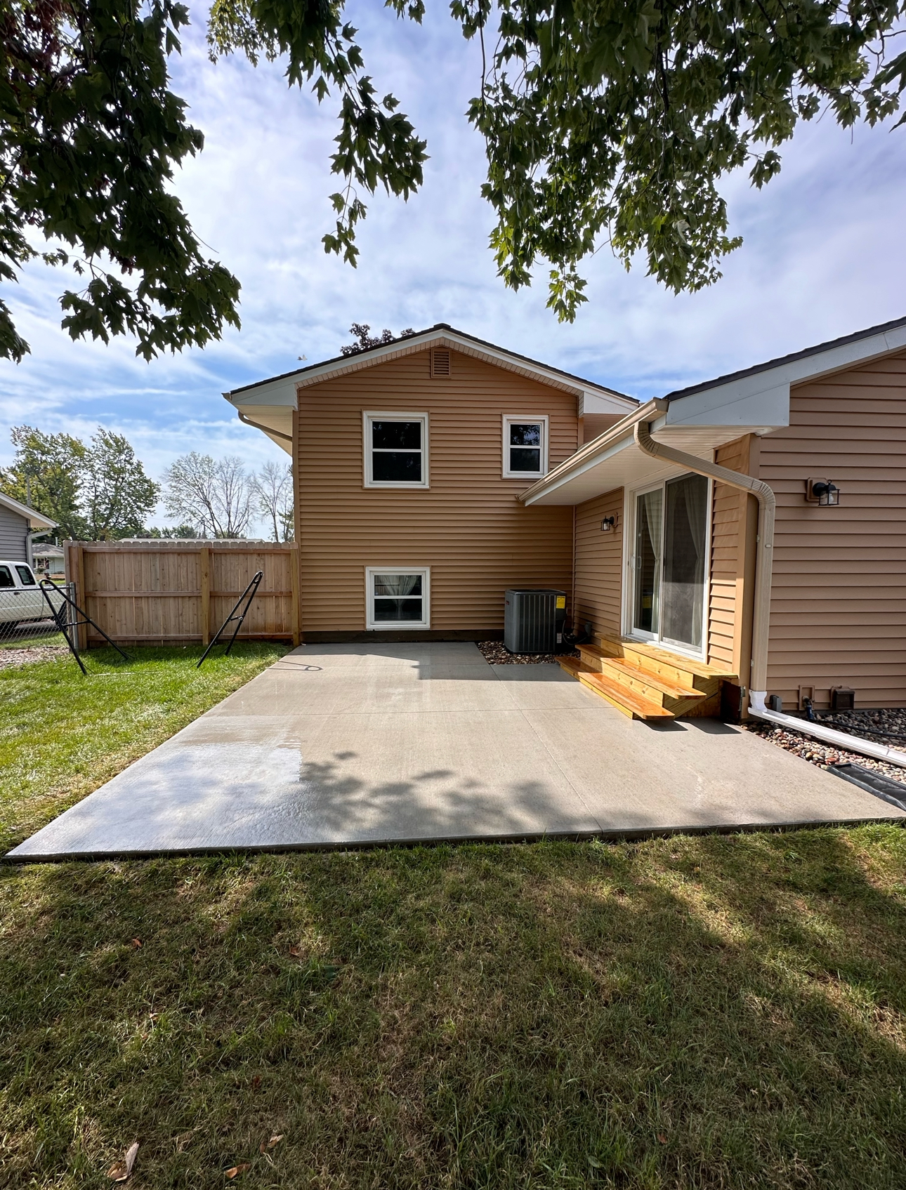 Freshly poured concrete patio in Des Moines, enhancing the backyard of a home with tan siding and a wooden fence.