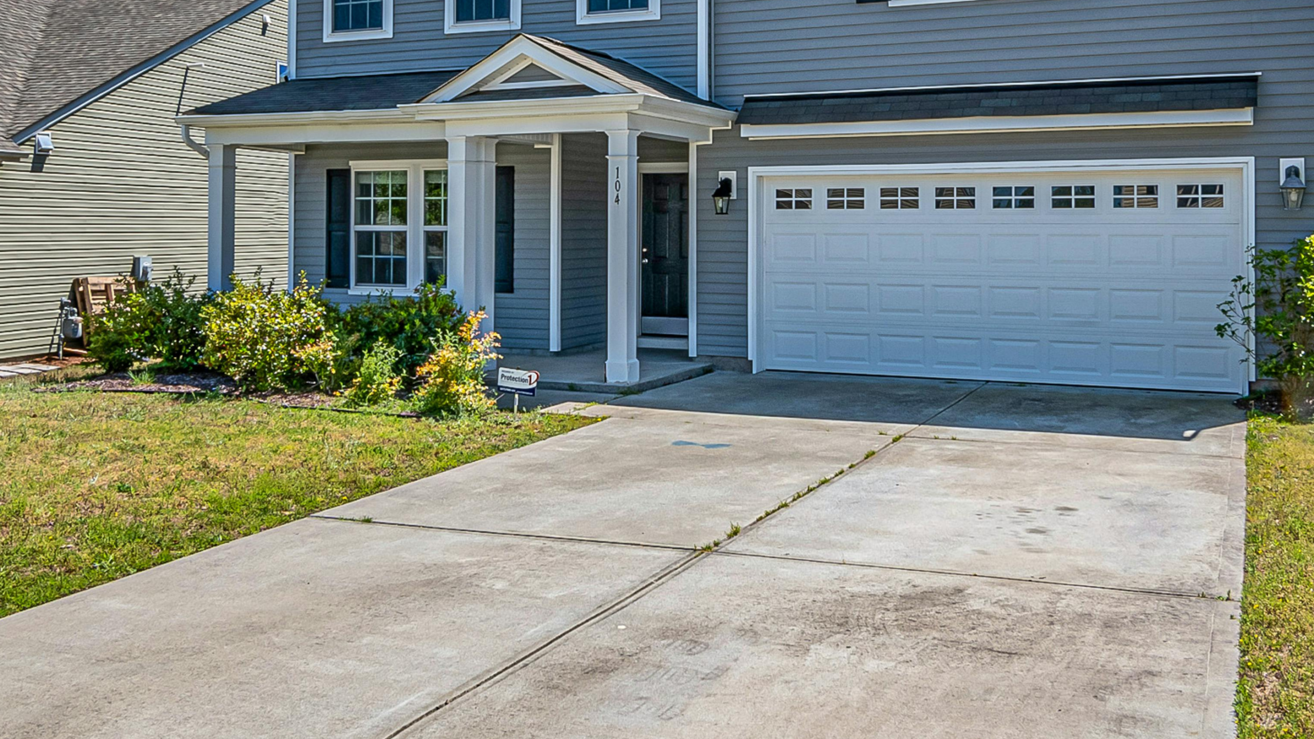 Concrete driveway leading to a gray house with a white garage door. Replace a driveway.